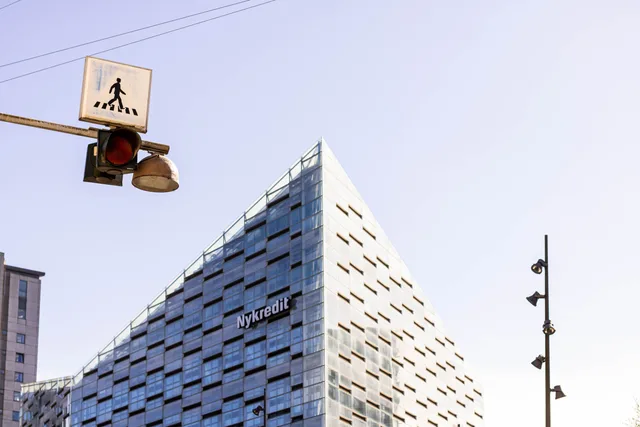 Low-angle view of Nykredit's modern building in Copenhagen under a clear sky. Hvilke faktorer påvirker lejen for kontorlokaler?